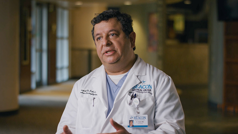 Male provider wearing lab coat talking, seating in room with glass doors behind him