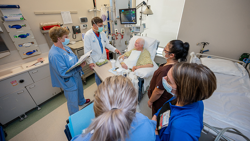 Group of providers stand around elderly male patient in ER exam room