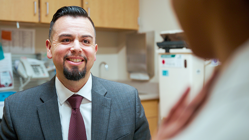 Male provider wearing a suit and tie, smiling at someone in exam room