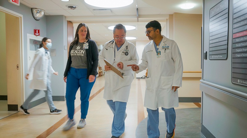 Two male doctors in lab coats and a female nurse walk down hospital corridor