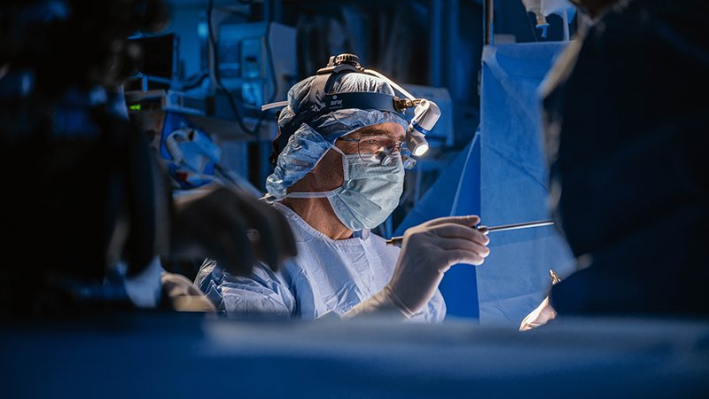 Surgeon in scrubs and lighted headgear working in operating room