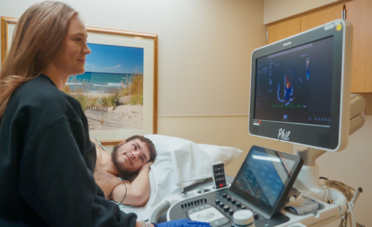 Male patient lying on his side, hooked to wires, watches as female technician runs a computer scan